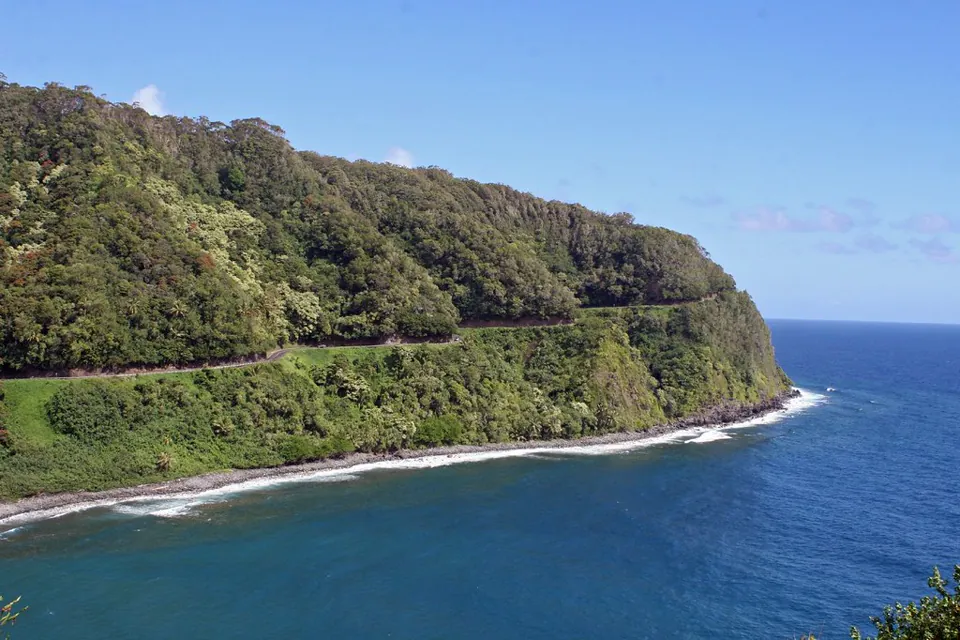 A coastal road crossing a green Hawaiʻi hillside above the ocean